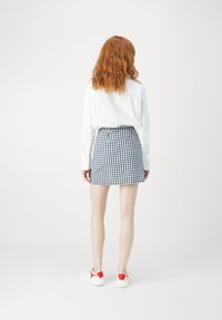 Schwarz-weißer Rock im Karo-Muster, hochgeschnitten, mit geradem Schnitt. Kombiniert mit weißen Sneakers mit roten Akzenten.