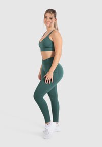 Sujetador deportivo verde oscuro y leggings de cintura alta, con una textura acanalada y diseño sin costuras, combinados con zapatillas deportivas blancas.
