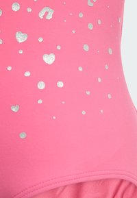 Rosa baddräkt med en slät textur, dekorerad med silverfärgade glittrande hjärtan och prickar över tyget för dekorativ detalj.