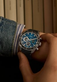 Timex Waterbury watch featuring a blue dial, silver-tone case, chronograph subdials, black leather strap, and tachymeter bezel.