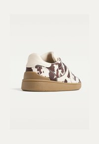 Kænguruskind sneakers med en kombination af brune og hvide teksturer, med en diskret tan sål og glatte læderdetaljer. Lavtop design vist fra siden.