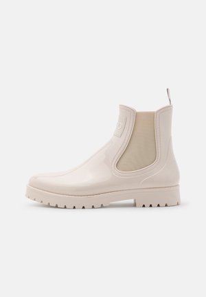 Beige waterdichte Chelsea-boots met een glanzende afwerking, elastische zijpanelen en een gestructureerde rubberen zool. Opvallende trekband aan de achterkant.
