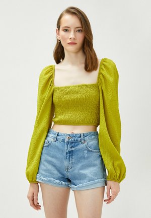Zielony, teksturowany crop top z bufiastymi rękawami, zestawiony z jasnoniebieskimi, zniszczonymi szortami denimowymi z postrzępionymi brzegami.