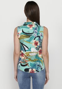 Bešvarkas mėlyna spalva su tropiniu gėlių raštu. Turi apykaklę, išlenktą apatinį kraštą ir lengvą, tekstūruotą audinį.