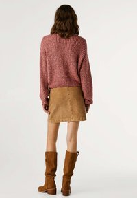 Πλεκτό πουλόβερ σε σκουρία απόχρωση με μακριά μανίκια, σε συνδυασμό με τζιν φούστα σε καφετί απόχρωση και καφέ σουέτ μπότες μέχρι το γόνατο. Ορατές λεπτομέρειες ραφής.