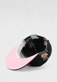 Musta ja vaaleanpunainen lippapipo, jossa on litteä lippa, brodeerattu sarjakuvakuvaus sisällä ja valkoinen vuori.