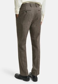 Braune Fischgrät-Hosen mit strukturierter Oberfl�äche, ausgestattet mitGesäßtaschen und einem geraden Bein-Design. Getragen mit schwarzen Schuhen.