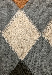 Szara dzianina z teksturowanymi diamentowymi wzorami w kolorach kremowym, brązowym i beżowym, z pętlami przędzy w obrębie diamentów.