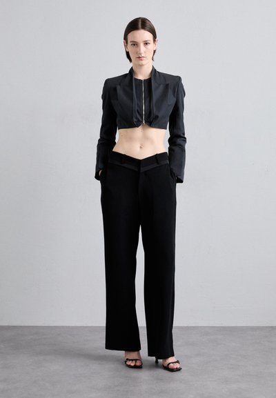 Black cropped jacket with a front zipper, paired with wide-leg black trousers featuring a unique folded waistband and flat shoes.