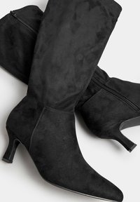Botas de ante negras hasta el tobillo con punta afilada, tacón bajo y detalle de cremallera lateral. La textura suave y el diseño elegante mejoran la apariencia general.