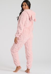 Roze fluffy onesie met een capuchon, gemaakt van textuurstof, met elastische mouwen en zakken. Het ontwerp bevat subtiele patronen op de stof.