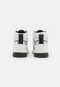 Høye sneakers i hvitt lær med svarte detaljer. Har en sølvstripe på siden, flat svart gummisåle og opphekkingsløkke på hælen.
