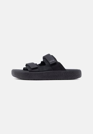 Schwarze Open-Toe-Pantoffel mit zwei verstellbaren Riemen und strukturierter Sohle, Seitenansicht auf weißem Hintergrund.