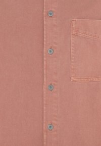 Koralowa koszula zapinana na guziki, wykonana z teksturowanej tkaniny, posiadająca sześć metalowych guzików oraz jedną kieszeń na piersi.