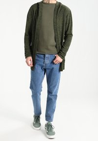 Felpa con cappuccio leggera e verde scuro a maniche lunghe sopra una maglietta abbinata, abbinata a jeans azzurri chiari e sneaker verdi. Vestibilità semplice e rilassata.