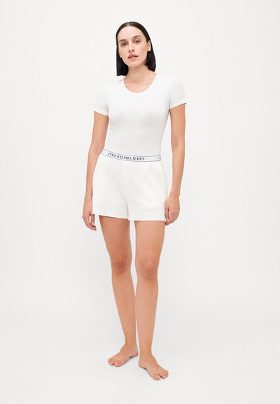 White short-sleeve bodysuit paired with cream shorts featuring a branded elastic waistband. Smooth texture, fitted design.