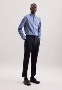 Camicia a maniche lunghe con motivo floreale blu e colletto button-down, abbinata a pantaloni neri su misura e scarpe stringate nere.