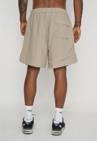 Pantalones cortos cargo beige con un bolsillo trasero, confeccionados en tela ligera. Cintura elástica con un ajuste holgado y detalles de costura visibles.