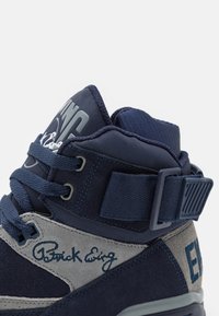 Baskets montantes en daim bleu marine et en mesh, avec des accents en daim gris, une fermeture à lacets, des détails signés et une sangle.