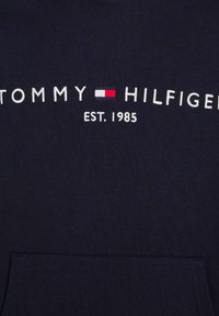 Felpa blu navy in cotone con tasca frontale. Presenta testo ricamato bianco: "TOMMY HILFIGER EST. 1985" con logo rosso e bianco.