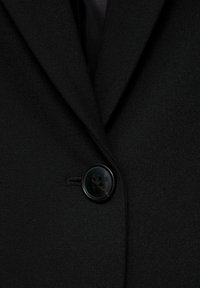 Gros plan de l'avant d'une veste de costume noire avec un seul bouton noir fermé et un col à revers cranté visible.