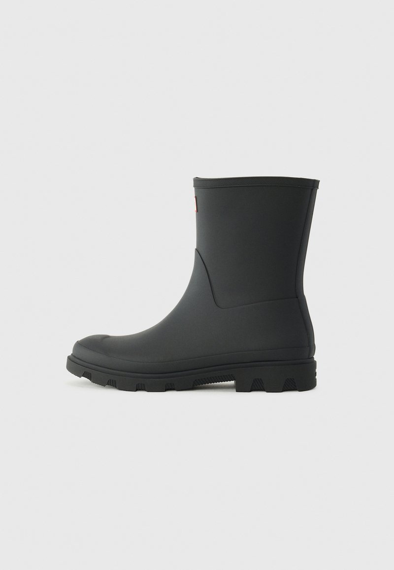 Botte noire en caoutchouc jusqu'à la cheville avec une texture lisse, un bout rond et une semelle à traction robuste. Présente une tige basse et un détail de logo sur le côté.