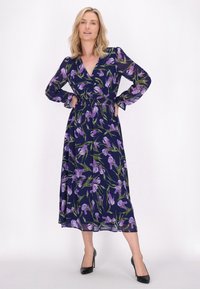 Rochie lungă, de culoare bleumarin, cu un model floral purpuriu, având mâneci lungi, un decolteu adânc în formă de V și talie strânsă. Este completată cu tocuri negre.