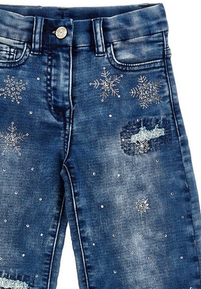 Jeans in denim di colore blu scuro con decorazioni in metallo a forma di fiocchi di neve sparsi e una toppa usurata. Presentano il tradizionale design a cinque tasche.