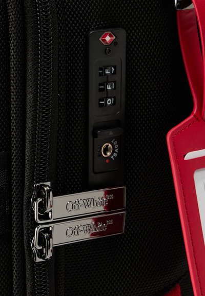 Φερμουάρ μαύρης υφασμάτινης βαλίτσας με ασημί τσέπες Off-White και κλειδαριά συνδυασμού εγκεκριμένη από TSA σε μαύρο πλαστικό πάνελ.