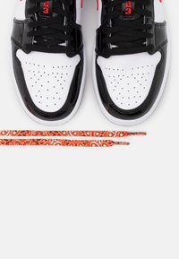 Zapatillas en blanco y negro con puntera perforada, acentos de charol negro y cordones naranjas con patrones que presentan remolinos y diseños florales.