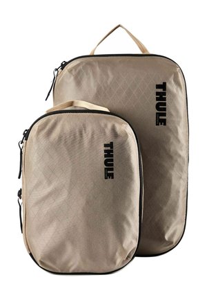 Due cubi da imballaggio rettangolari beige con cerniere e maniglie nere, con il logo verticale nero "THULE" su sfondo bianco.