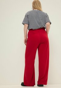 Czerwone spodnie z szerokimi nogawkami o gładkiej fakturze, zestawione z czarno-białym paskowanym topem z krótkim rękawem. Widoczne tylne kieszenie na spodniach.