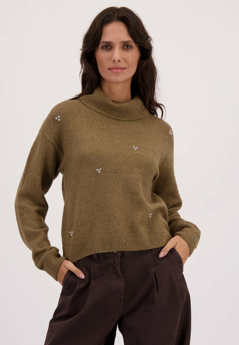 Olijfgroene trui met hoge kraag, voorzien van een zachte textuur, brede mouwen en kleine zilveren versieringen door de stof.