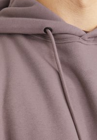 Light mauve hoodie made of soft cotton blend. Features a drawstring with black aglets and ribbed cuffs, showcasing smooth texture.