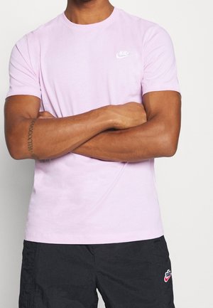 Jasnoróżowa bawełniana koszulka z krótkimi rękawami, dekoltem typu crewneck i białym logo Nike na lewej piersi. Model złożone ręce na przodzie.