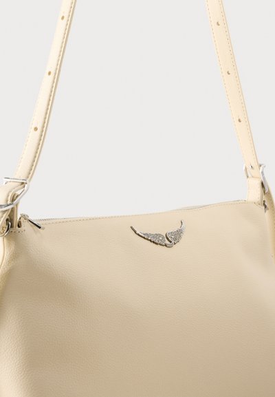 Μπεζ δερμάτινη τσάντα ώμου με ρυθμιζόμενο λουρί, ασημένιο φερμουάρ και διακοσμητικό ασημένιο έμβλημα σε σχήμα φτερού μπροστά.