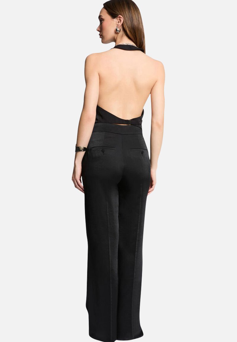Combinaison halter noire sans dos avec un bustier ajusté et un pantalon à jambes larges, présentant une texture lisse et deux poches arrière.