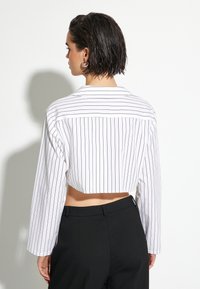 Kkort vit skjorta med svarta vertikala ränder, långa ärmar, krage och design med ryggpanel. Matchad med åtsittande svarta byxor.