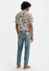 Camiseta de manga corta color crema con estampado gráfico negro; combinada con jeans azul claro y zapatillas naranjas, con parche de cuero en la cintura.