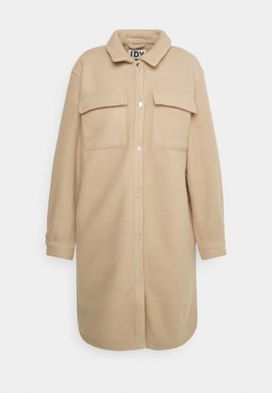 Beige Fleece-Hemdjacke mit Kragen, zwei Brusttaschen und Druckknopfverschluss. Lange Ärmel mit knöpfbaren Manschetten.