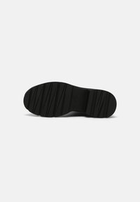 Black rubber shoe sole with a textured surface and ridged patterns for traction. Rounded toe and flat heel design. Durable and flexible material.