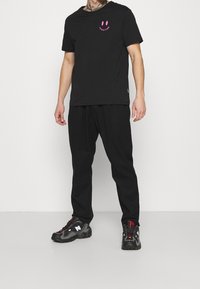 Černé tričko s růžovou grafikou usmívajícího se obličeje; kombinované s volnými černými kalhotami a černými teniskami s červenými akcenty. Neformální, bez vzoru.