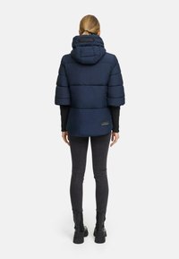Marineblauwe pufferjack met een capuchon, korte mouwen en een iets getailleerd silhouet. Matte textuur met een klein logo-label op de achterkant.
