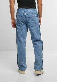 Hellblaue Denim-Jeans mit einem lockeren Schnitt, ausgestattet mit seitlichen Druckknopfverschlüssen, klassischen Gesäßtaschen und einer glatten Textur.