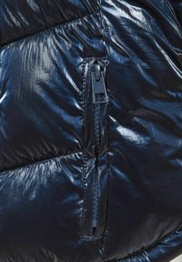 Tamnoplava puf jakna, sjajna i kviltana, s bočnom rajsferšlus džepom s glatkim zatvaranjem.