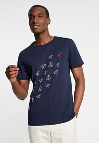 Marineblå bomull T-skjorte med en rekke papirflydesign i hvitt, med et rødt aksent. Korte ermer og rund hals.