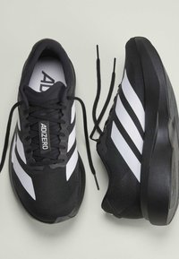 Scarpe da corsa Adidas Adizero nere e bianche con tre strisce bianche, lacci neri e suola spessa, viste dall'alto e dal lato.