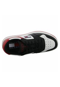 Sneaker nera, bianca e rossa con tomaia in pelle, punta forata e linguetta con marchio. Presenta una suola in gomma texturizzata e dettagli a contrasto.