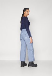 Light blue cargo pants with pockets, adjustable waistband, and subtle stitching details, worn with black ankle boots and a long-sleeve top.