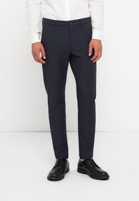 Pantaloni slim-fit navy dintr-un material neted, cu față plată, bucle pentru curea și închidere cu un singur nasture. Purtați cu pantofi din piele negri.